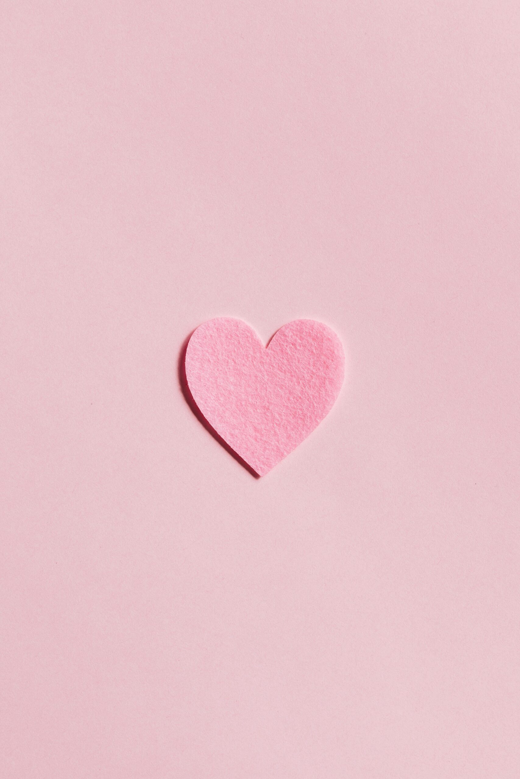 A simple pink felt heart on a light pink background, perfect for Valentine's Day themes.